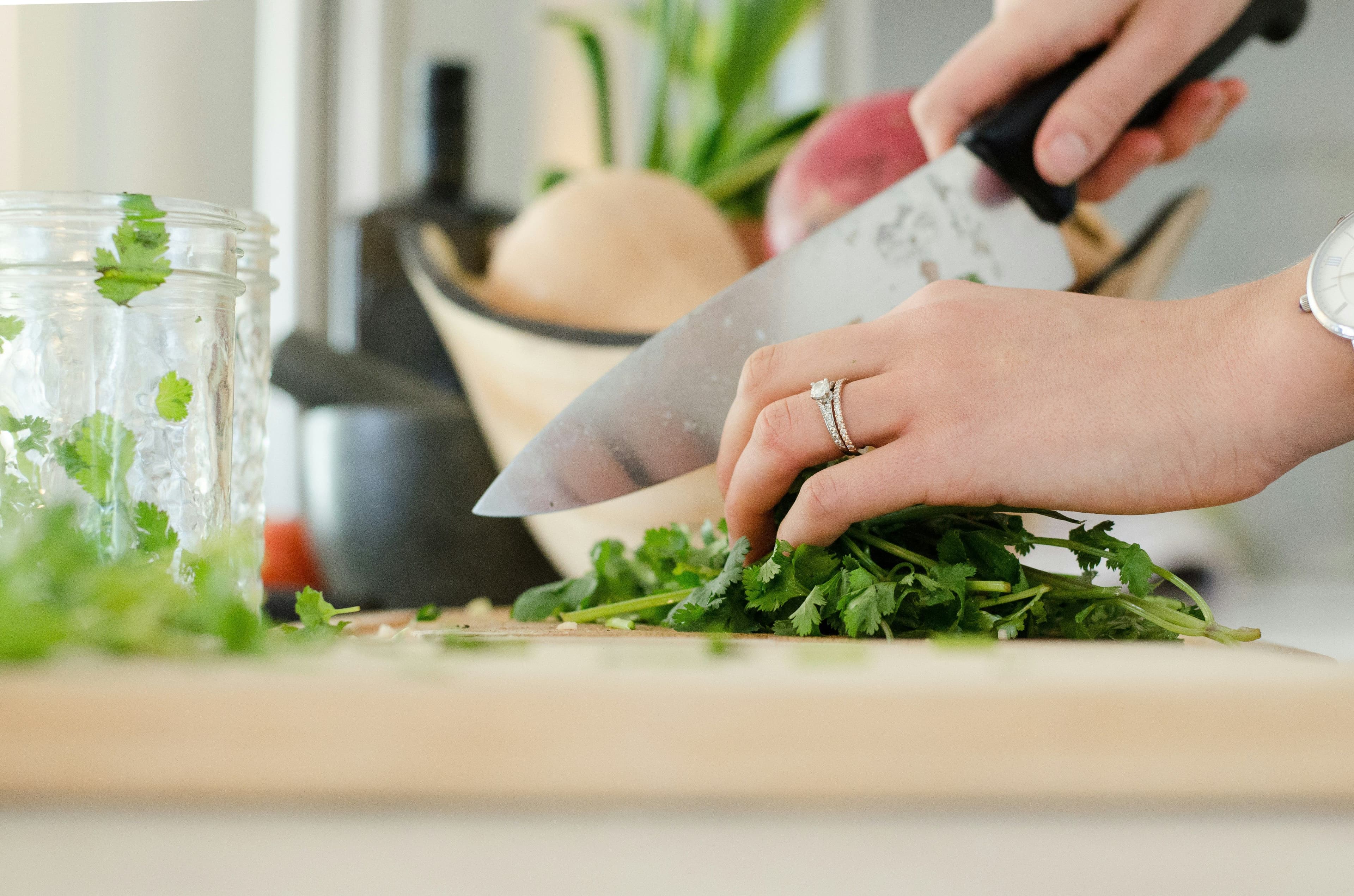 A side view of a hand chopping vegetables on a cutting board in the kitchen